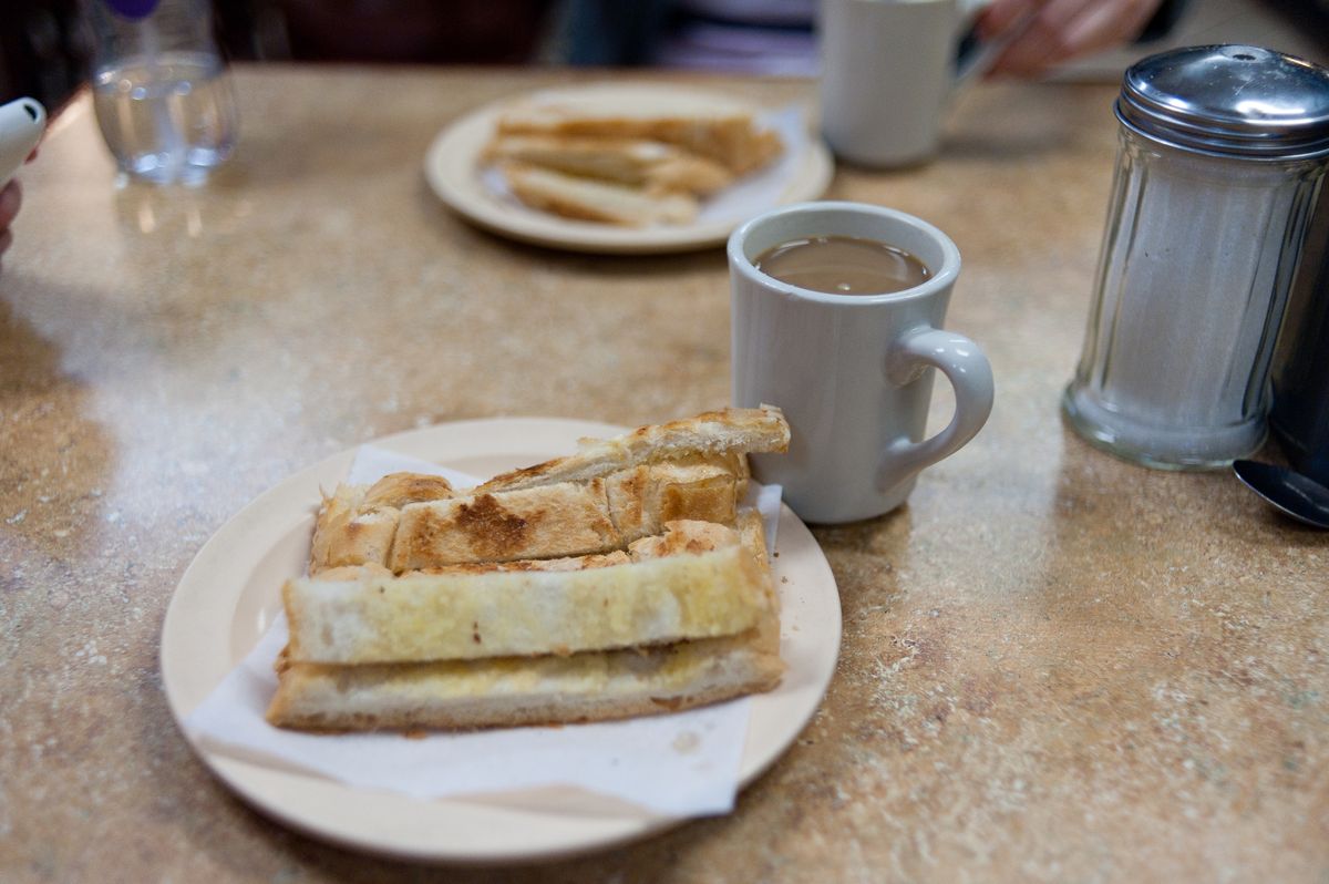 A cup of cafe con leche next to a plate of buttered tostadas at a Puerto Rican cafeteria