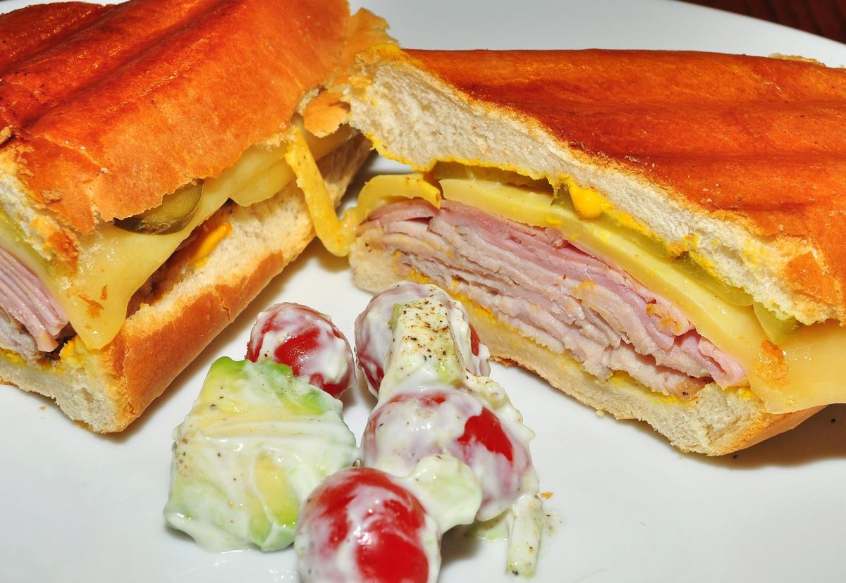 A pressed Cubano sandwich sliced in half, showing layers of ham, roast pork, cheese, and pickles